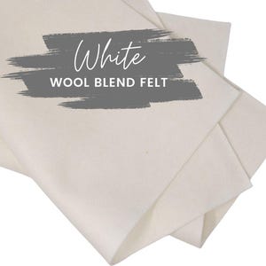 May include: White wool blend felt fabric, folded and layered. The text "White" is written in cursive above the text "WOOL BLEND FELT" in a gray rectangle.