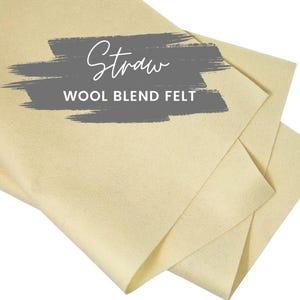 May include: A close-up of a folded piece of straw colored wool blend felt. The text "Straw Wool Blend Felt" is written in white on a gray background.