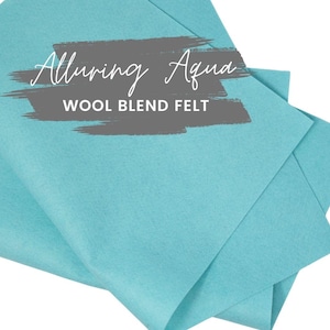 May include: Aqua-colored wool blend felt sheets. The image features several folded sheets of felt in a vibrant, light blue hue. Text on the felt reads "Alluring Aqua" and "Wool Blend Felt."