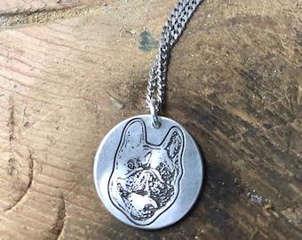 May include: A silver-colored pendant necklace featuring a detailed engraving of a dog's face. The pendant is circular and hangs from a delicate chain. The dog's features are clearly defined, showcasing the breed's characteristics.