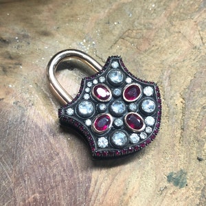 May include: A gold padlock with a black and silver design. The padlock is decorated with small red and white gemstones.
