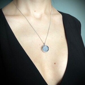 Op de afbeelding: Een zilveren ketting met een ronde hanger met het astrologische symbool voor Steenbok. De hanger is zilver met een zwarte achtergrond en het symbool is wit.