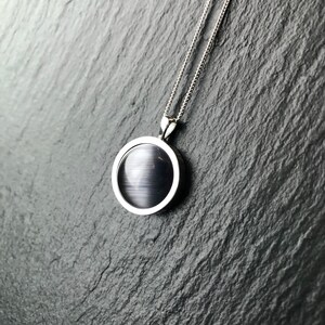 Op de afbeelding: Een zilveren ketting met een zwarte ovale hanger. De hanger heeft een glad, glanzend oppervlak.