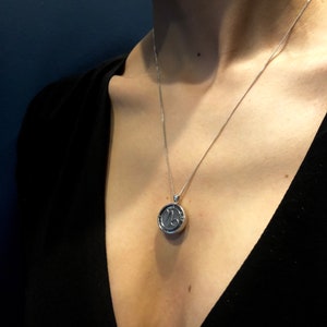 Op de afbeelding: Een zilveren ketting met een ronde hanger met het astrologische symbool voor Steenbok.