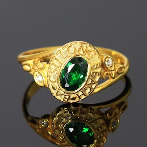 Op de afbeelding: Een gouden klasring met een groene ovale edelsteen en de inscriptie "SULTANA BEACH" rond de band.