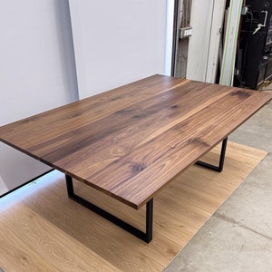 May include: A large, rectangular dining table with a natural wood top and black metal legs. The table is made of walnut wood and has a rustic, farmhouse style.