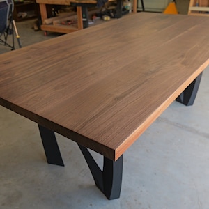 May include: A large, rectangular dining table with a dark brown walnut wood top and black metal legs. The table is made of solid wood and has a natural finish.