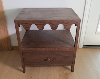 May include: A dark brown wooden end table with a single drawer and an open shelf. The table has a unique scalloped design on the top edge.