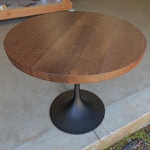 May include: A round wooden table top with a black pedestal base. The table top is made of walnut wood and has a natural finish.
