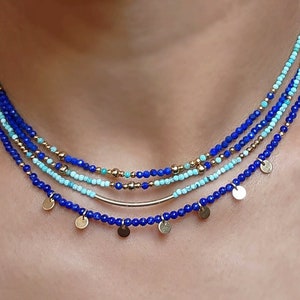 May include: A layered necklace with blue and turquoise beads and gold accents. The necklace has small gold discs hanging from the bottom.