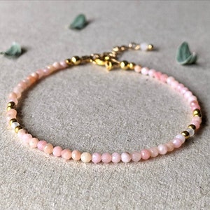 May include: A delicate pink opal gemstone bracelet with gold accents. The bracelet is made with small, round beads and has a simple, elegant design.