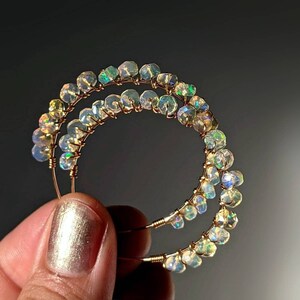 May include: Gold hoop earrings with iridescent opal beads. The earrings are double-layered and have a delicate wire design.