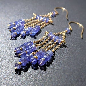 May include: A pair of gold dangle earrings with multiple strands of small, light blue gemstones. The earrings have a simple, elegant design.