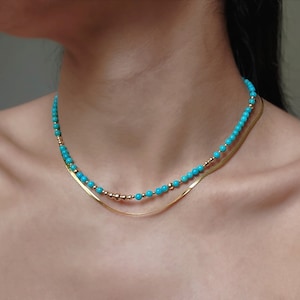 May include: A layered necklace with a turquoise beaded chain and a gold chain. The turquoise beads are small and round.