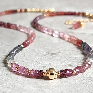 May include: A necklace with a gradient of pink, purple, and red gemstones. The necklace has a gold clasp and small gold beads. The gemstones transition from darker to lighter shades, creating a visually appealing accessory.