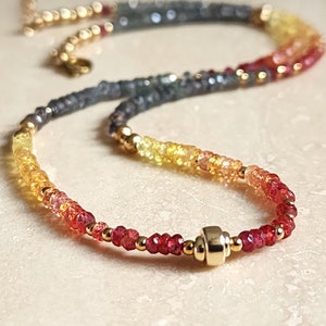 Puede incluir: Un delicado collar con un degradado de piedras preciosas coloridas, que va del rojo intenso al amarillo y gris. El collar está adornado con pequeñas cuentas doradas y un cierre dorado. Ideal para añadir un toque de elegancia.