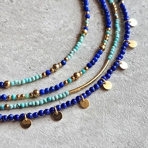 May include: A layered necklace with blue and turquoise beads and gold accents. The necklace features small gold discs hanging from the bottom.