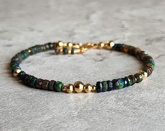 May include: A beaded bracelet featuring faceted dark green and black beads with gold-colored accents. The bracelet has a gold-colored clasp and three larger gold-colored beads in the center. A piece of jewelry.