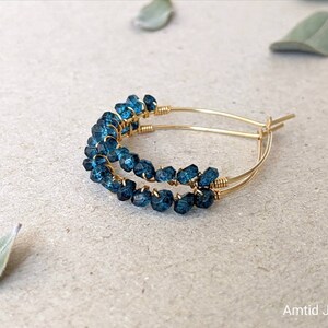 May include: Gold hoop earrings with blue gemstone beads. The earrings are made with wire wrapped around the beads.