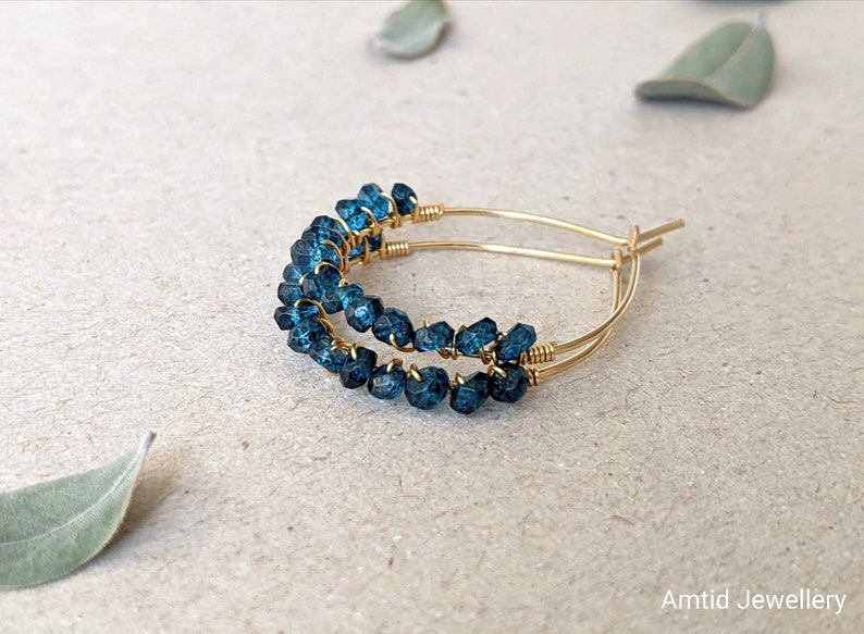 May include: Gold hoop earrings with blue gemstone beads. The earrings are made with wire wrapped around the beads.