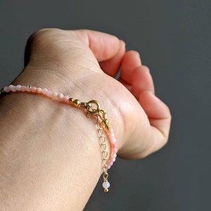 May include: A delicate bracelet made with small pink opal beads and gold accents. The bracelet has a lobster clasp closure and an adjustable chain.