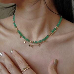 May include: A gold chain necklace with a layered strand of green gemstone beads and small gold disc charms.