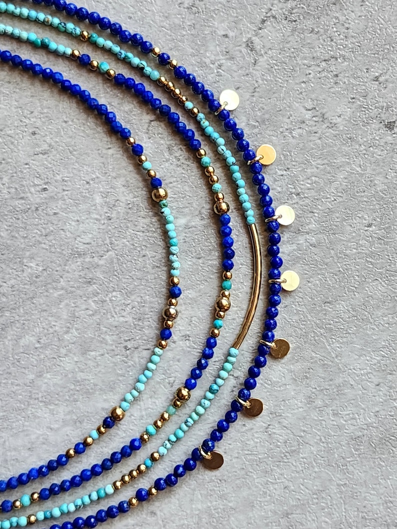 May include: A set of four layered necklaces featuring blue and turquoise gemstone beads and gold accents. The necklaces are adorned with small gold discs.