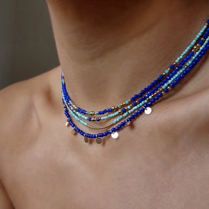 May include: A layered necklace with blue and turquoise beads and gold accents. The necklace has small gold discs hanging from it.