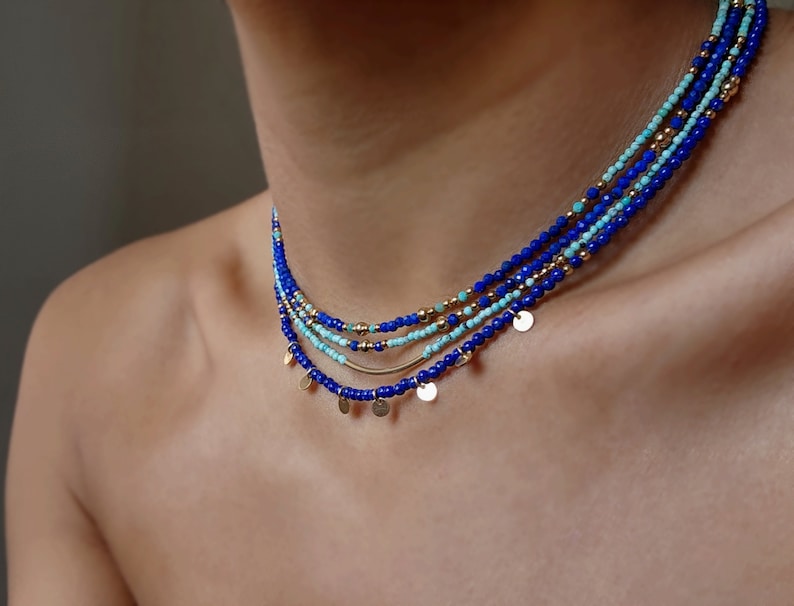 May include: A layered necklace with blue and turquoise beads and gold accents. The necklace has small gold discs hanging from it.