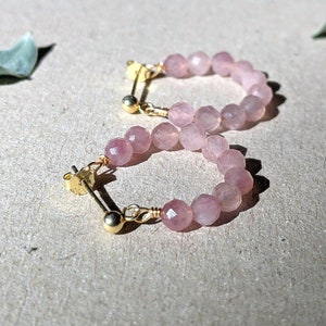 May include: A pair of gold hoop earrings with pink gemstone beads. The earrings are made of delicate wire and feature a simple design.