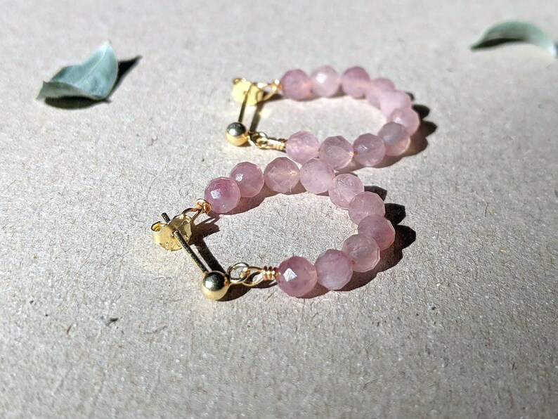 May include: A pair of gold hoop earrings with pink gemstone beads. The earrings are made of delicate wire and feature a simple design.