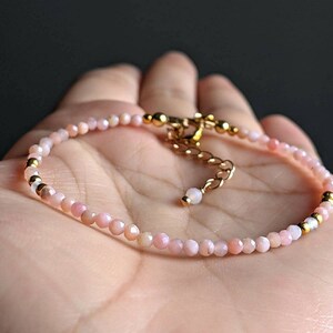 May include: A delicate pink opal gemstone bracelet with gold accents. The bracelet features small, round beads and a gold clasp.