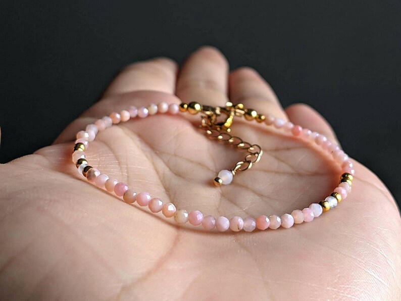 May include: A delicate pink opal gemstone bracelet with gold accents. The bracelet features small, round beads and a gold clasp.