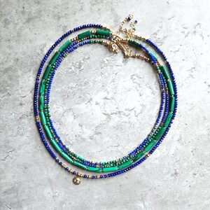 May include: A layered necklace with blue and green beads. The necklace has a gold chain and a small gold charm.