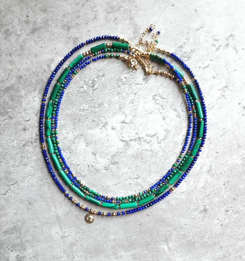 May include: A layered necklace with blue and green beads. The necklace has a gold chain and a small gold charm.