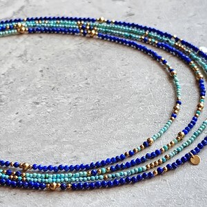 May include: Multi-strand necklace with blue and turquoise beads and gold accents. The necklace features a layered design with small, round beads and gold spacers.