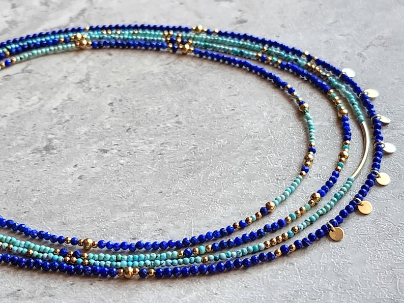 May include: Multi-strand necklace with blue and turquoise beads and gold accents. The necklace features a layered design with small, round beads and gold spacers.