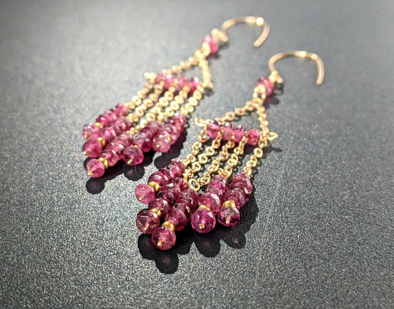 Puede incluir: Pendientes de oro con un dise&ntilde;o en cascada de piedras preciosas rosas. Los pendientes son largos y colgantes, con varias hileras de peque&ntilde;as piedras rosas.