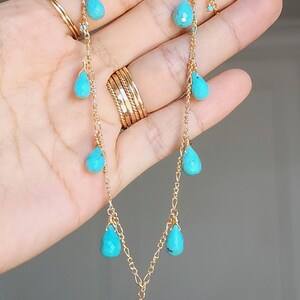 May include: A delicate gold necklace featuring teardrop-shaped turquoise stones. The necklace has a fine chain with multiple turquoise pendants of varying sizes, creating a cascading effect. The gold chain and turquoise stones are the focal points.