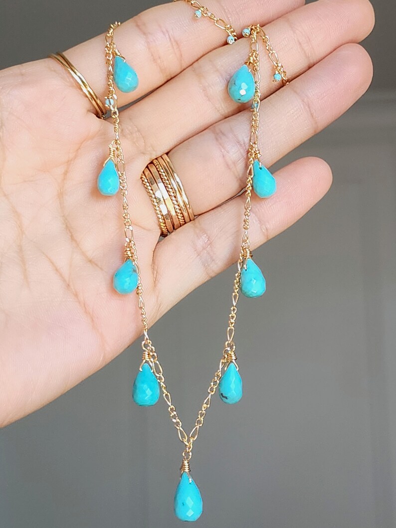 May include: A delicate gold necklace featuring teardrop-shaped turquoise stones. The necklace has a fine chain with multiple turquoise pendants of varying sizes, creating a cascading effect. The gold chain and turquoise stones are the focal points.