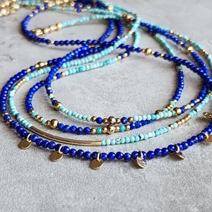 May include: A layered necklace with blue and turquoise beads and gold accents. The necklace features a silver bar and small gold charms.