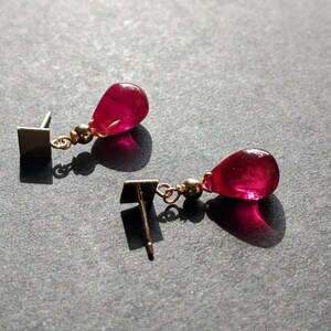 May include: A pair of earrings with a teardrop-shaped red gemstone and a gold-coloured metal setting.