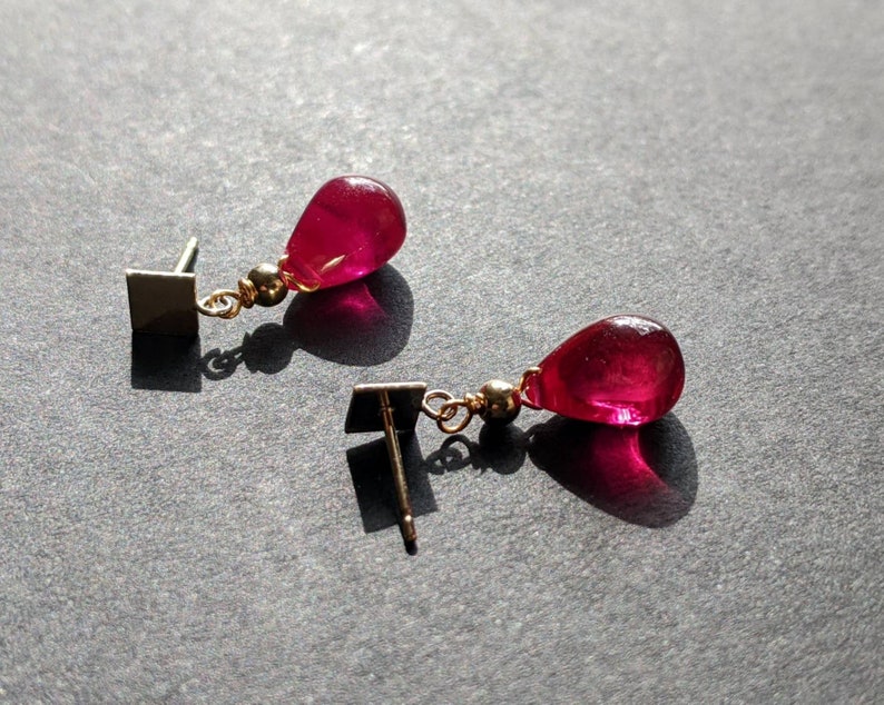 May include: A pair of earrings with a teardrop-shaped red gemstone and a gold-coloured metal setting.