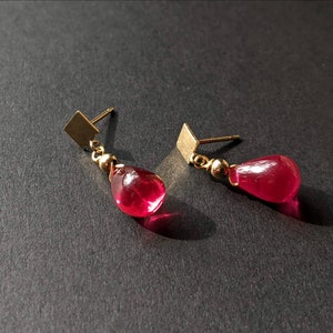 May include: A pair of gold earrings with teardrop-shaped red glass stones.