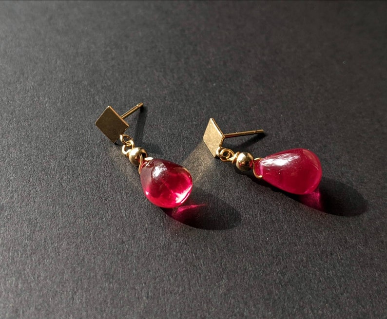 May include: A pair of gold earrings with teardrop-shaped red glass stones.