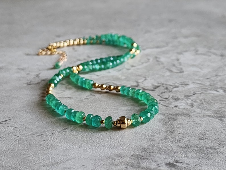 May include: A delicate green gemstone necklace with gold beads. The necklace is made with small, faceted green stones and gold beads, and has a gold clasp.