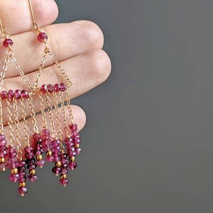 Puede incluir: Pendientes de oro con un dise&ntilde;o triangular y m&uacute;ltiples hileras de cuentas de piedras preciosas rosas.