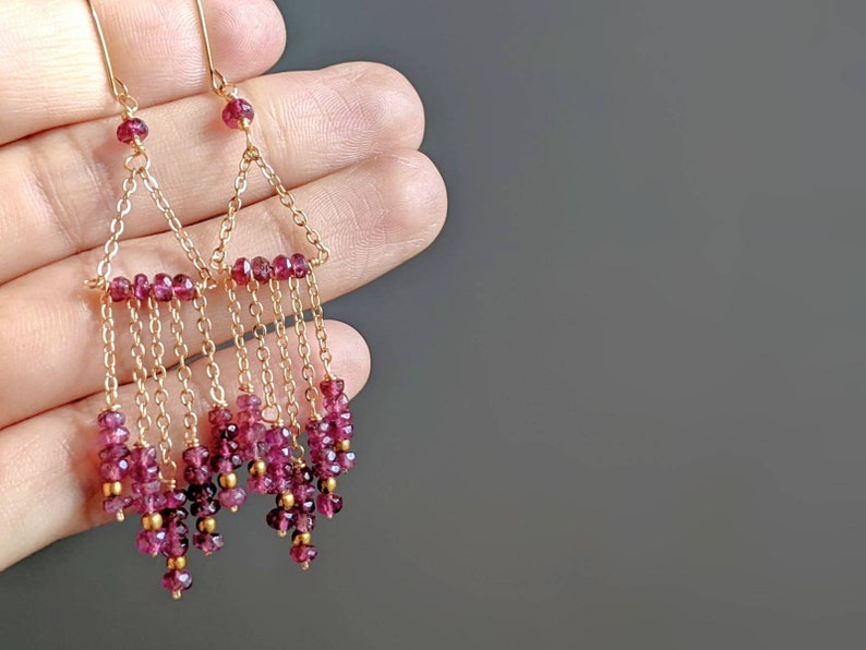 Puede incluir: Pendientes de oro con un dise&ntilde;o triangular y m&uacute;ltiples hileras de cuentas de piedras preciosas rosas.