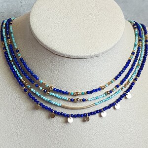 May include: A layered necklace with blue and turquoise beads and gold accents. The necklace has small gold discs hanging from it.