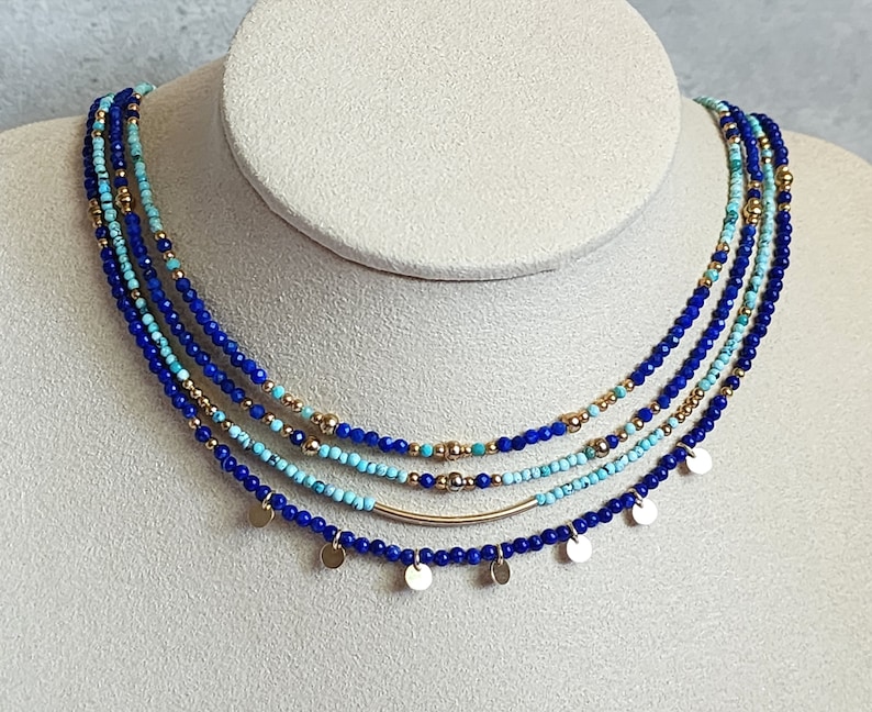 May include: A layered necklace with blue and turquoise beads and gold accents. The necklace has small gold discs hanging from it.